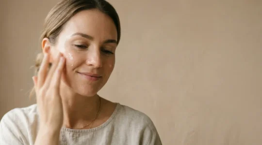 Donna con pelle luminosa e idratata che applica siero viso su sfondo minimalista