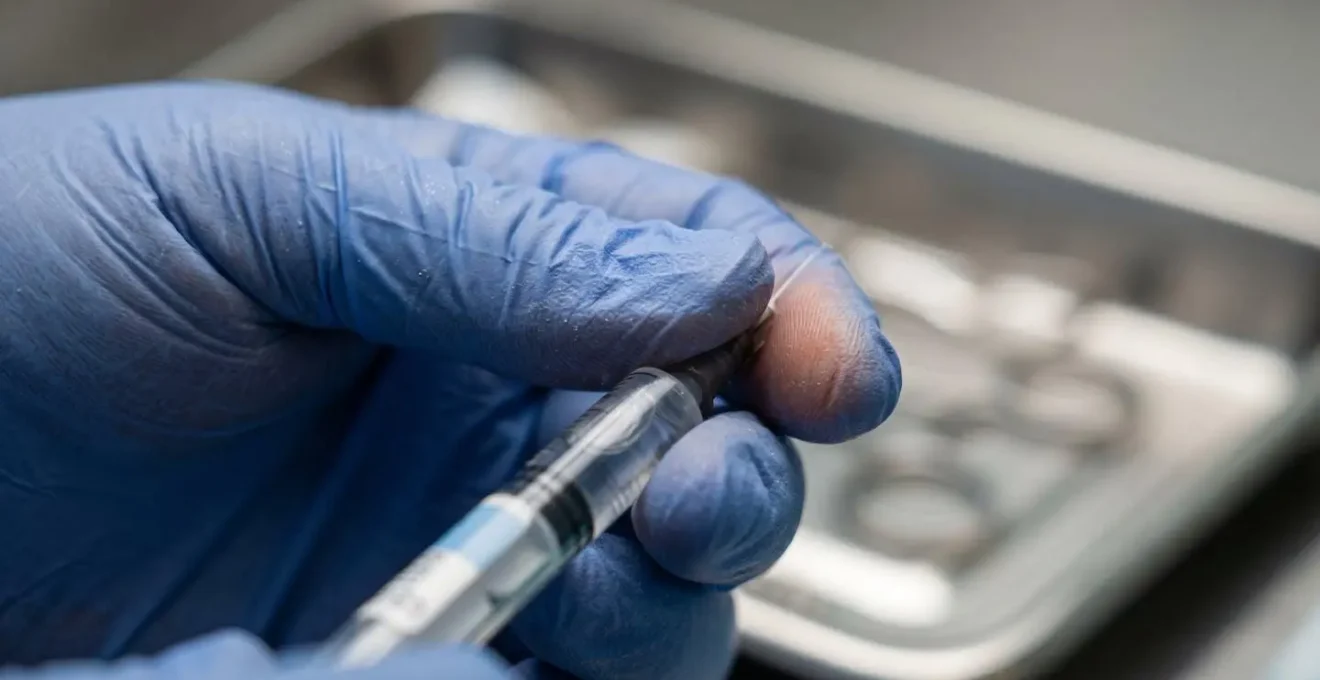 Dettaglio macro delle mani di un professionista medico durante la preparazione sicura di un trattamento iniettabile