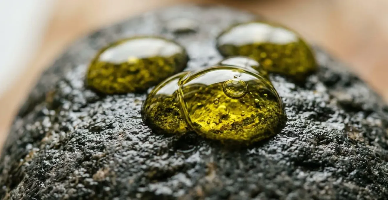 Dettaglio macro di gocce dorate di olio extravergine di oliva su superficie naturale che evidenzia texture e purezza