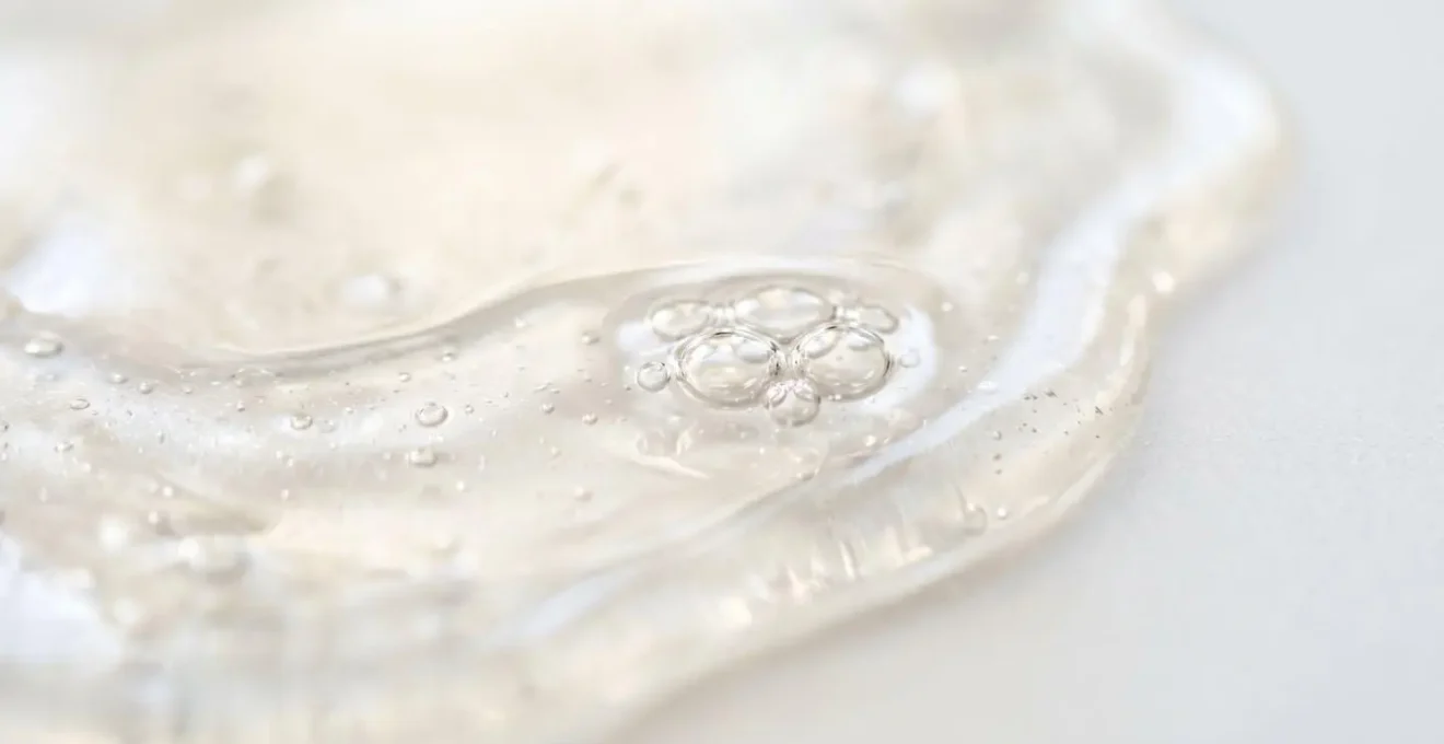 Macro estremo di texture cremosa e luminosa di un siero cosmetico con gocce trasparenti, focus su dettagli molecolari e riflessi